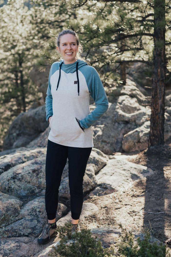 Women's fleece pullover hoodie with cream body and dusty blue raglan sleeves, worn outdoors