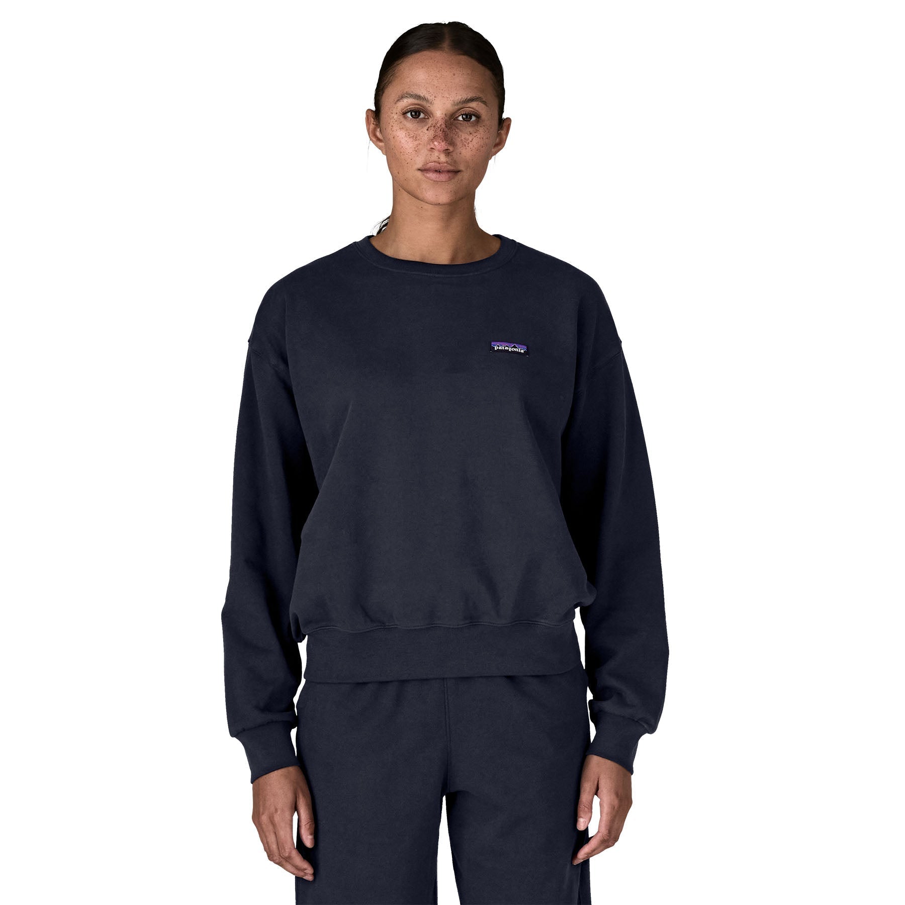 Women's dark navy crewneck sweatshirt with small chest logo patch, front view on model